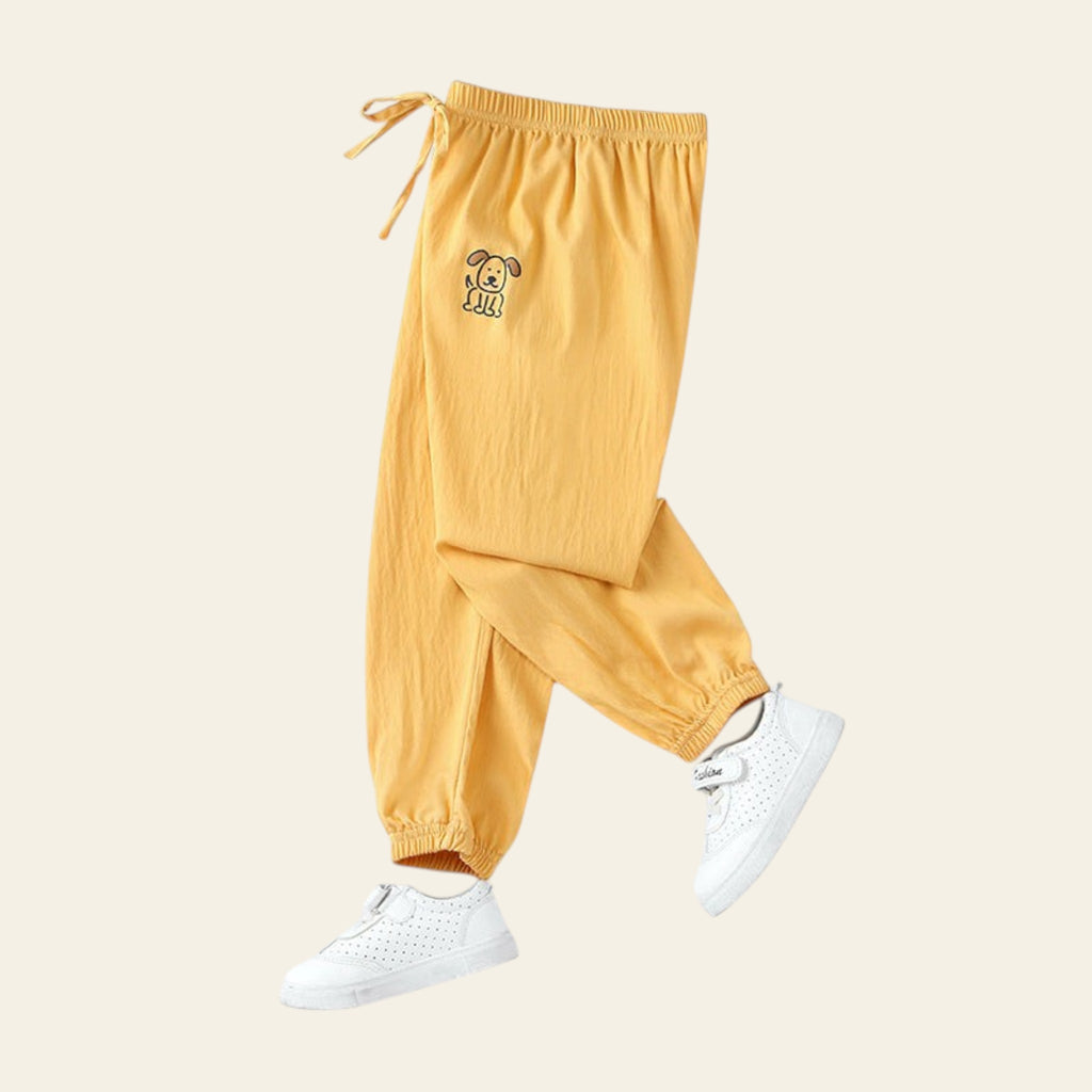 Yellow pants with a small logo worn by a person, on a white background with a small plant and smiley face decoration.