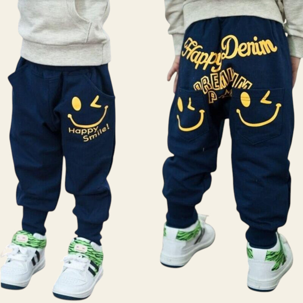 Navy blue pants with smiley face designs and 'Happy Denim' text worn by a person on a wooden floor.