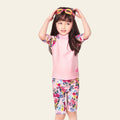 Child wearing a pink floral outfit with sunglasses on a white background