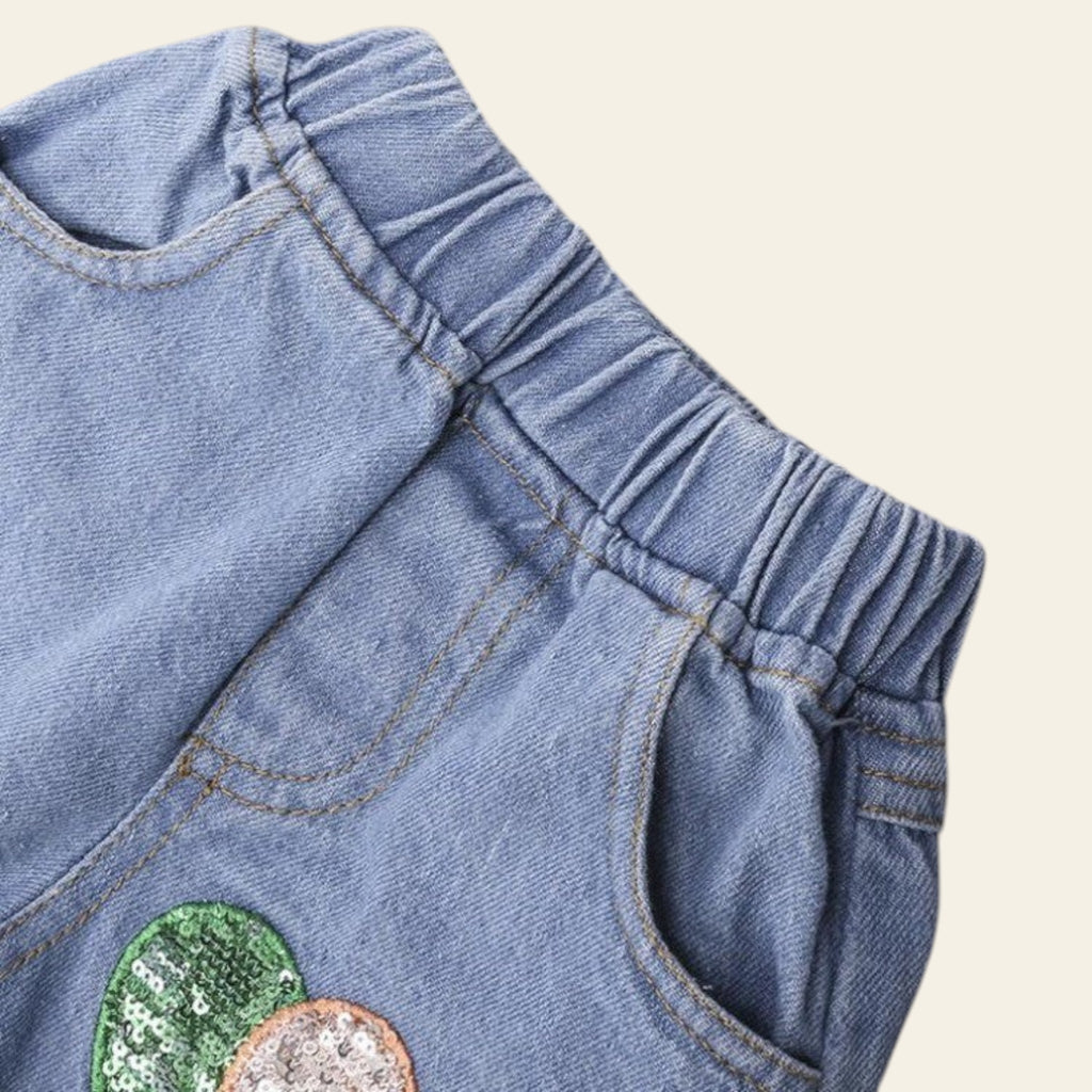 Close-up of denim pants with a green and gold sequin patch on a gray background