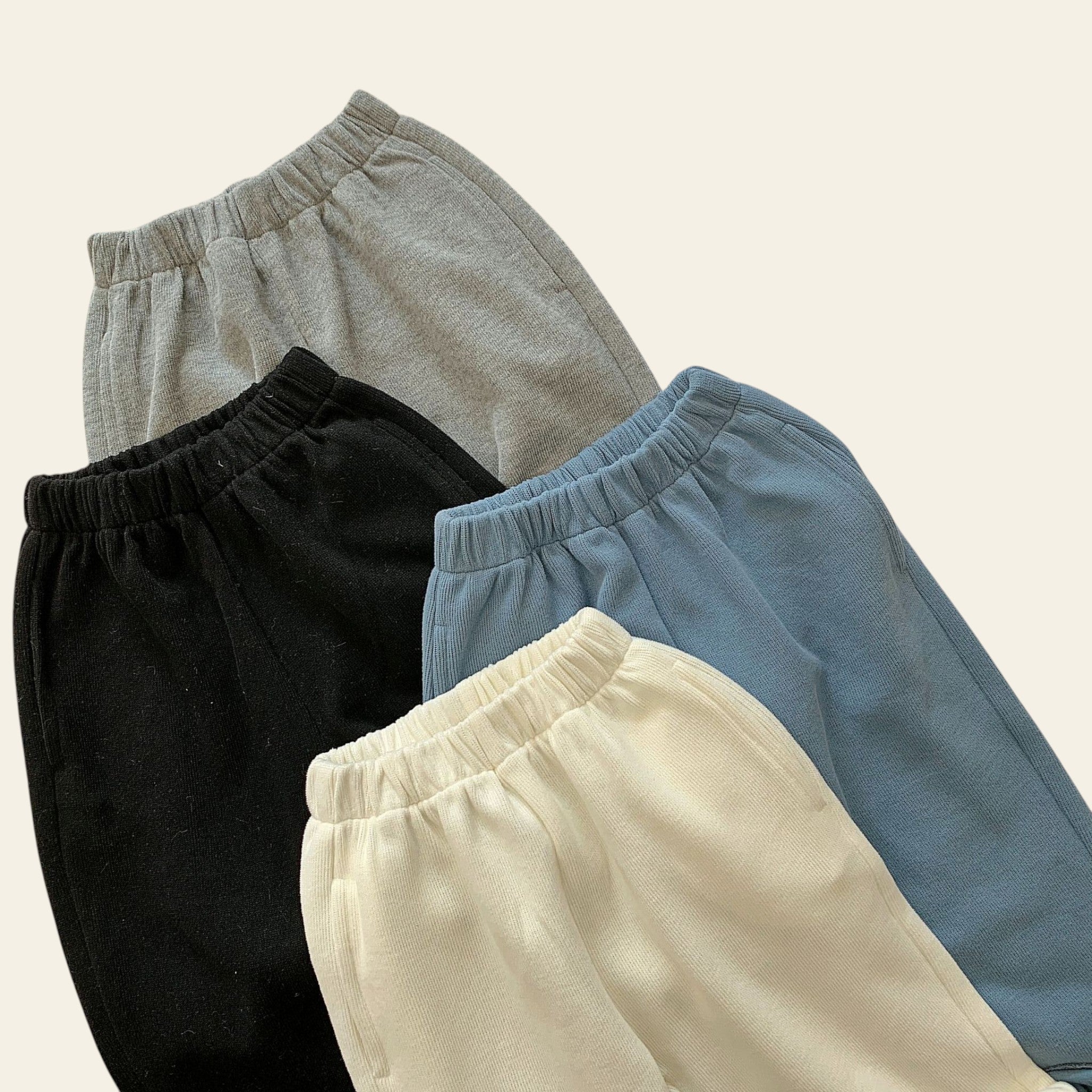 Four pairs of pants in gray, black, beige, and blue on a textured surface.