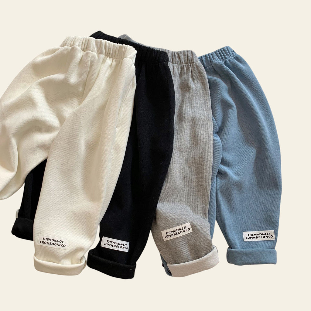Four pairs of pants in white, black, gray, and blue on a textured surface.