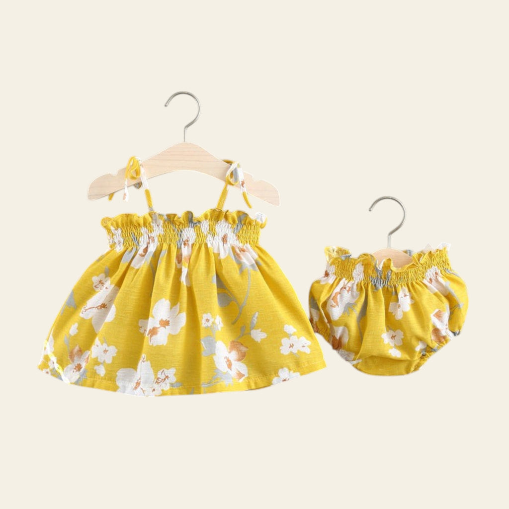 Yellow floral baby dress and bloomers set on hangers against a gray background