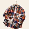 Plaid shirt with text on a wooden surface with toys and flowers in the background