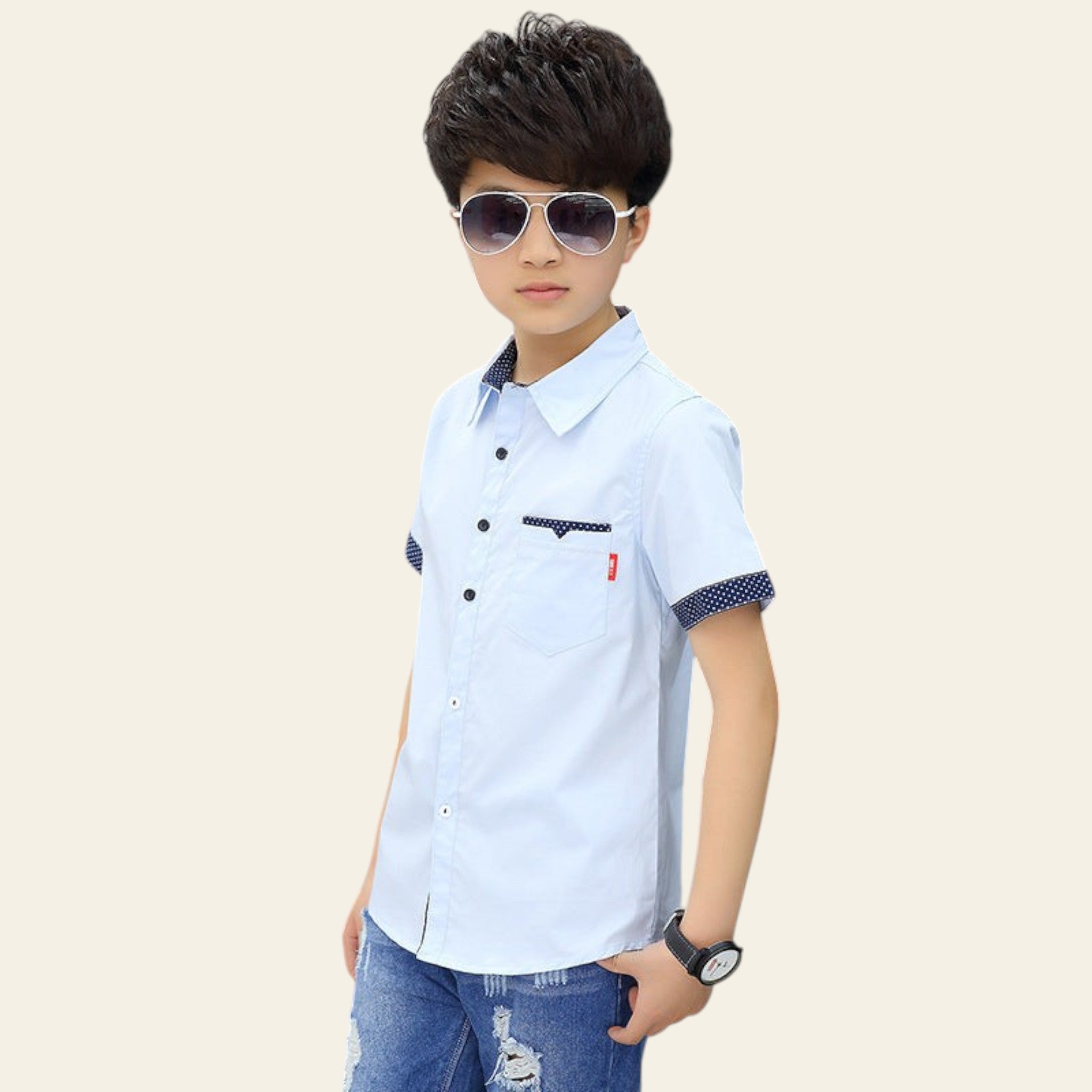 Young boy wearing a white short-sleeve shirt with blue accents and sunglasses, standing outdoors.