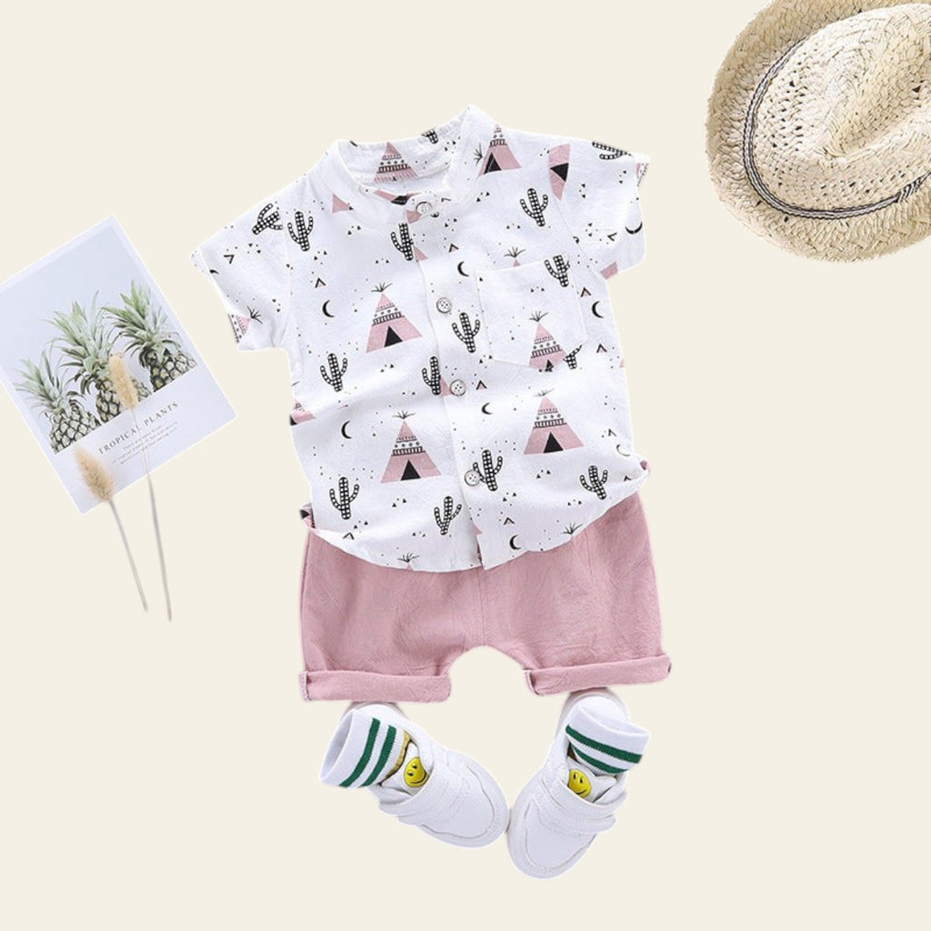 Children's outfit with white shirt and pink shorts, accompanied by a hat and shoes on a gray background.