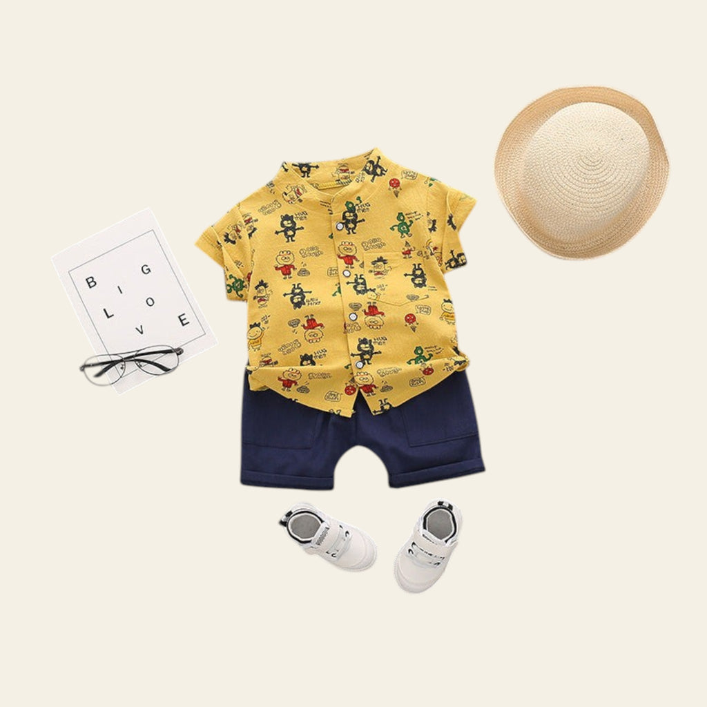 Children's outfit with yellow shirt, navy shorts, white shoes, and straw hat on a gray background.