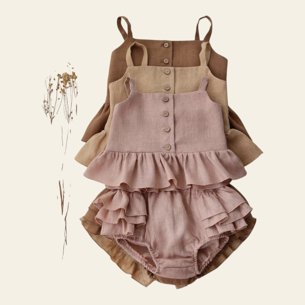 Children's ruffled dress and overalls set on a white background with dried flowers.