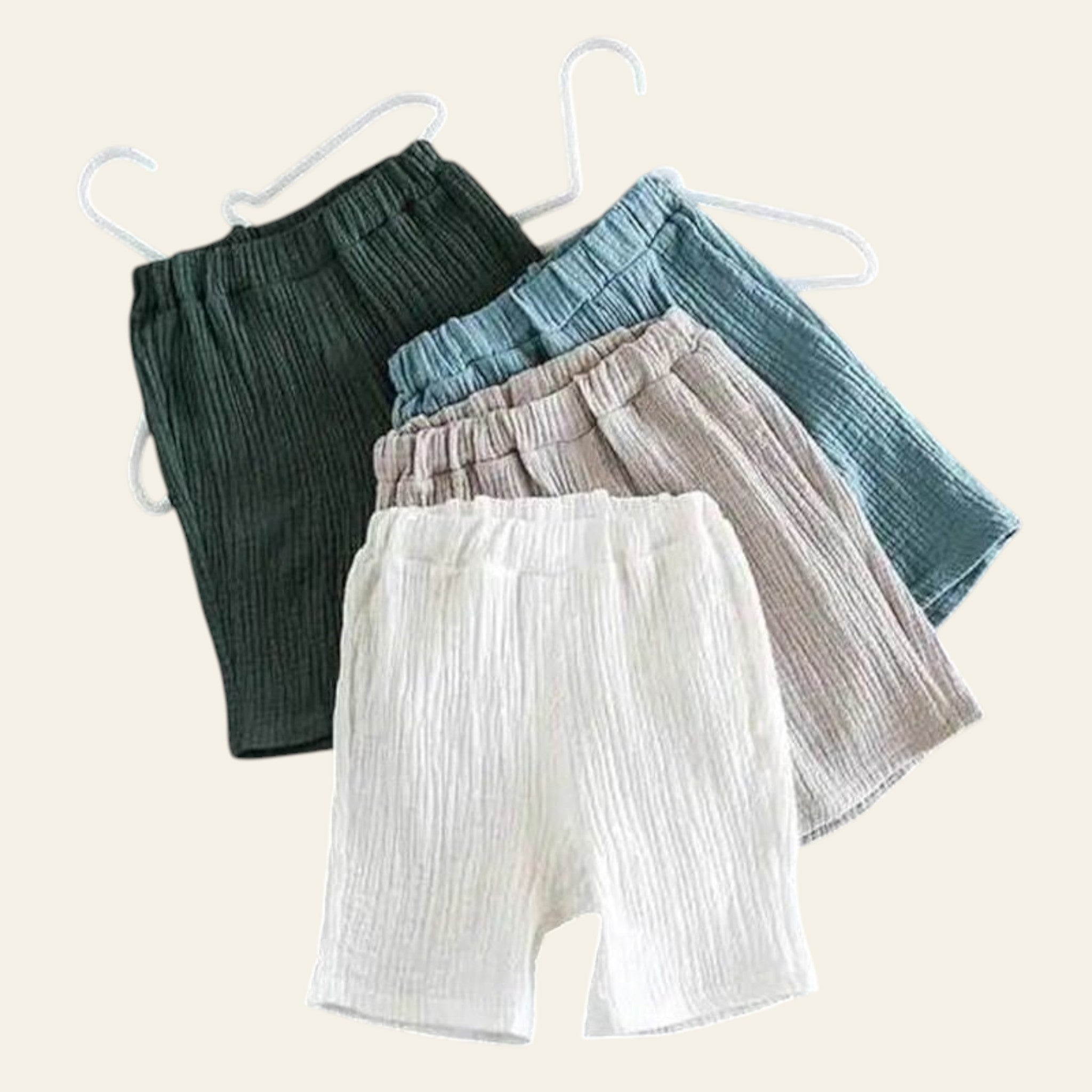 Three pairs of pants in green, blue, and white hanging on a gray background.