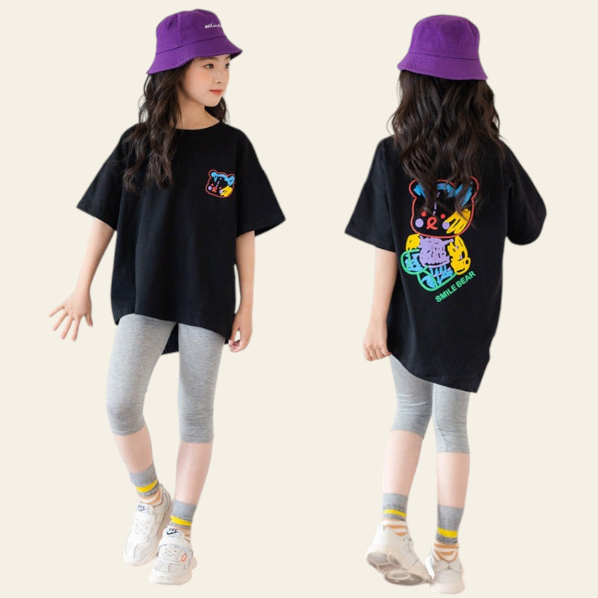 Two children wearing matching black t-shirts with colorful designs, gray leggings, and purple hats against a white paneled wall.