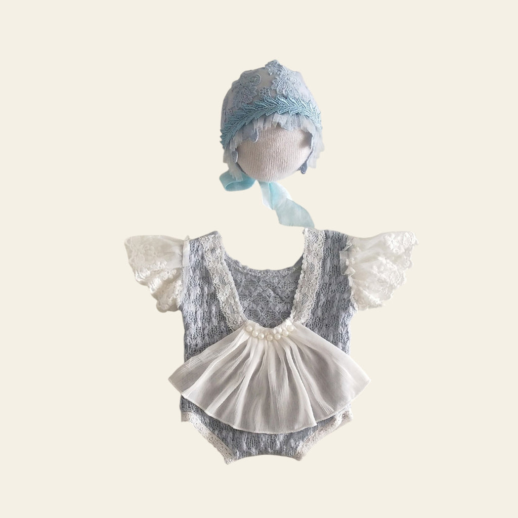 Baby romper with lace details and matching bonnet on a light background