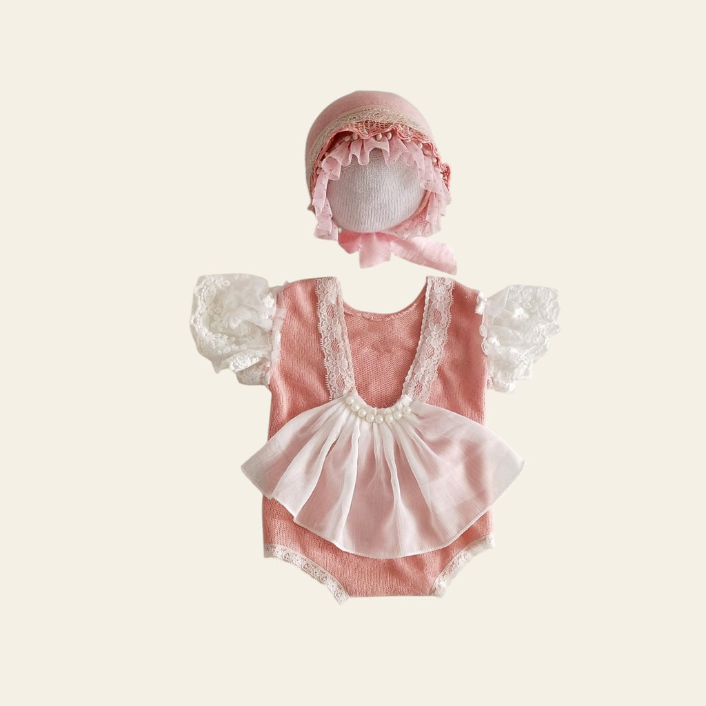 Pink baby romper with lace details and matching bonnet on a light gray background