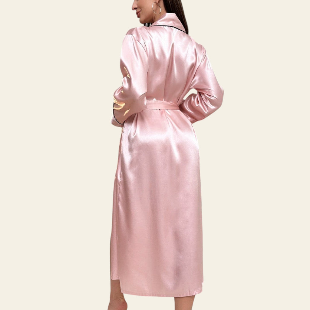 Woman wearing a pink satin robe in a stylish room with a couch and large window.