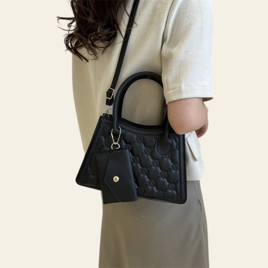 Person holding a black quilted handbag in an indoor setting