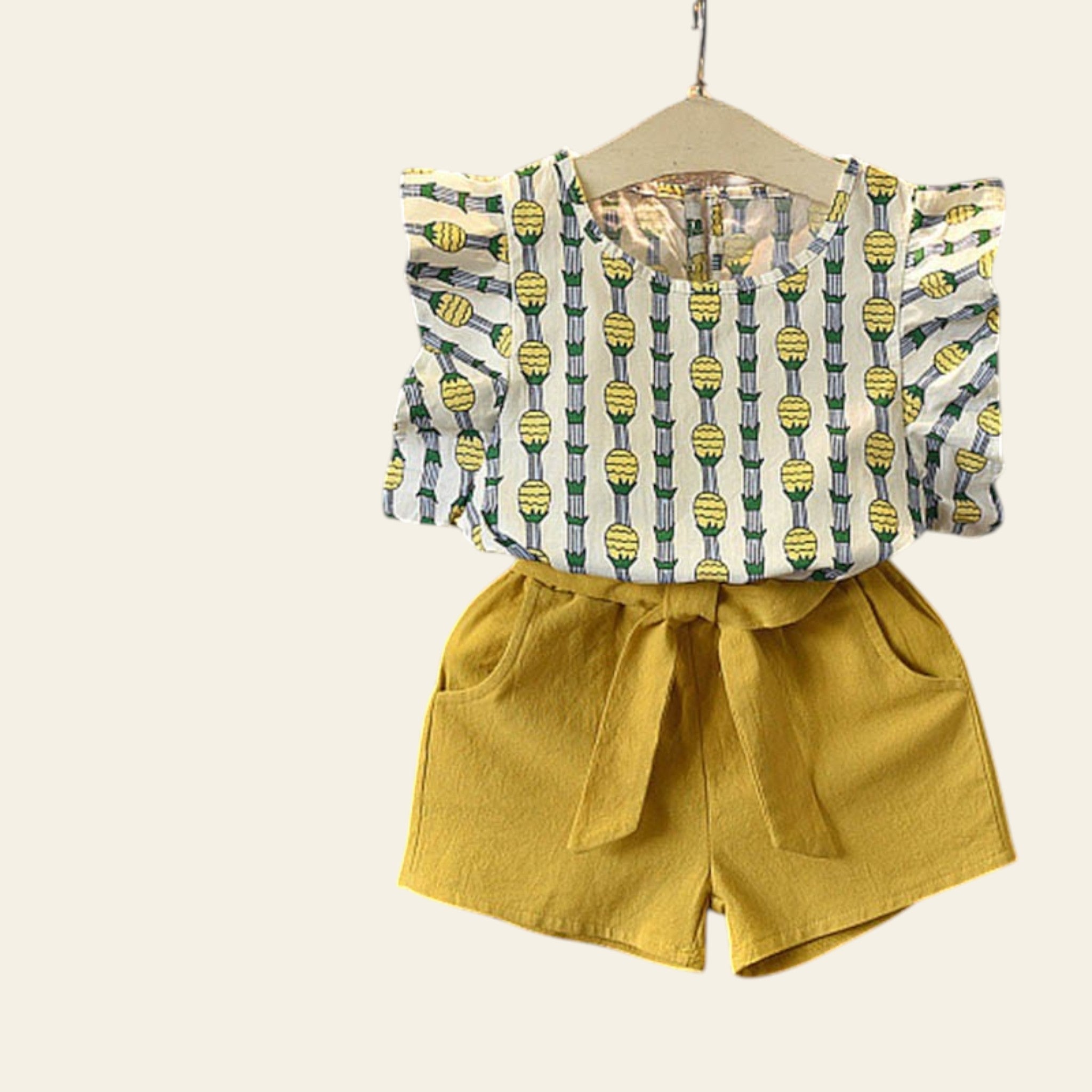 Children's outfit with patterned top and yellow shorts on a gray background with flowers.