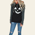 Person wearing a black hoodie with a pumpkin face design, standing indoors.