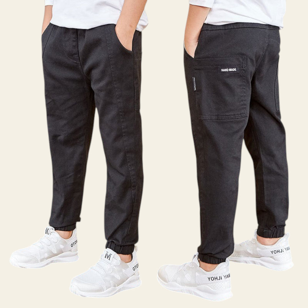 Two pairs of black pants with white sneakers on a wooden floor.