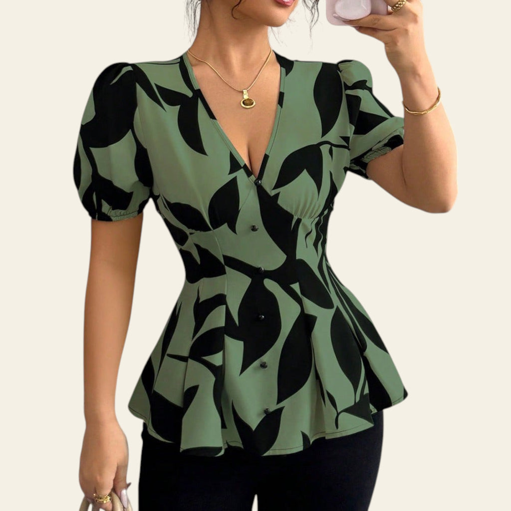 Woman wearing a green and black leaf-patterned blouse taking a mirror selfie.