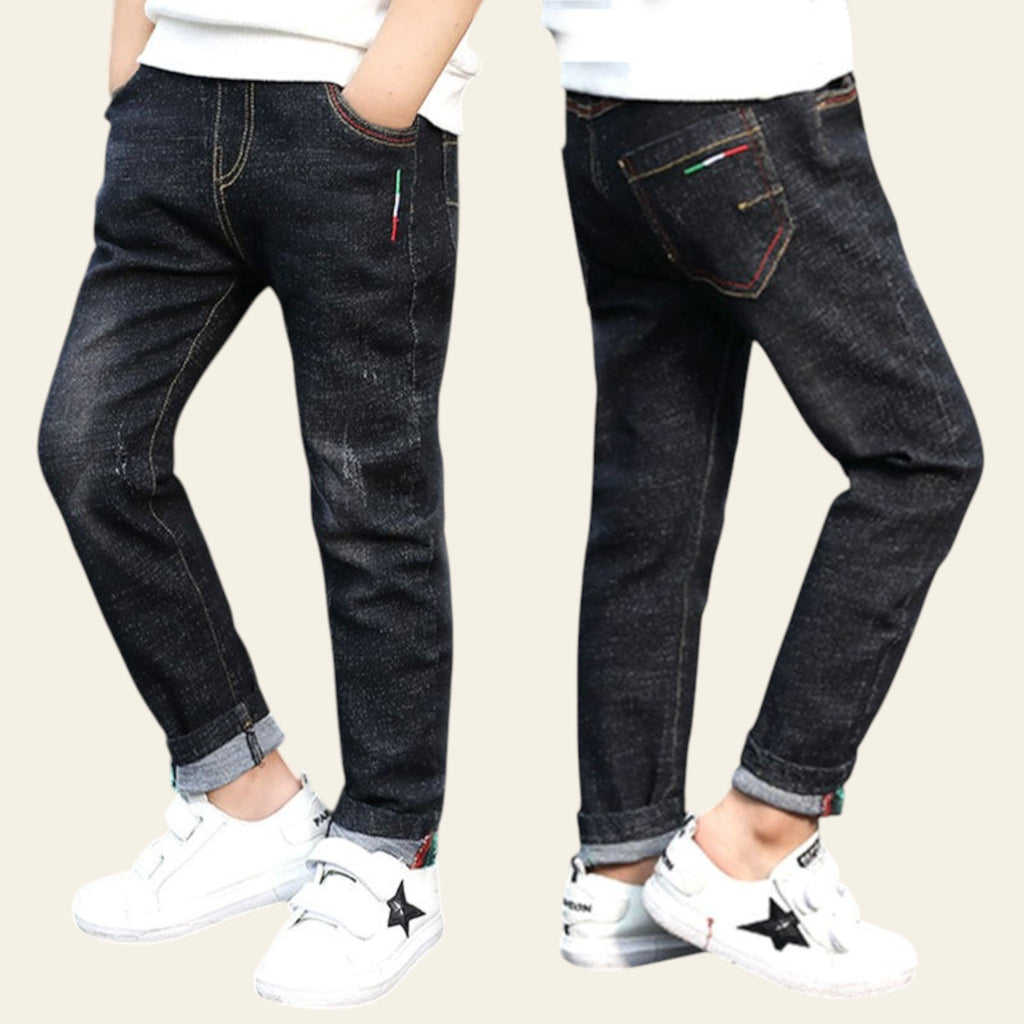 Two pairs of dark jeans worn by children on a street.