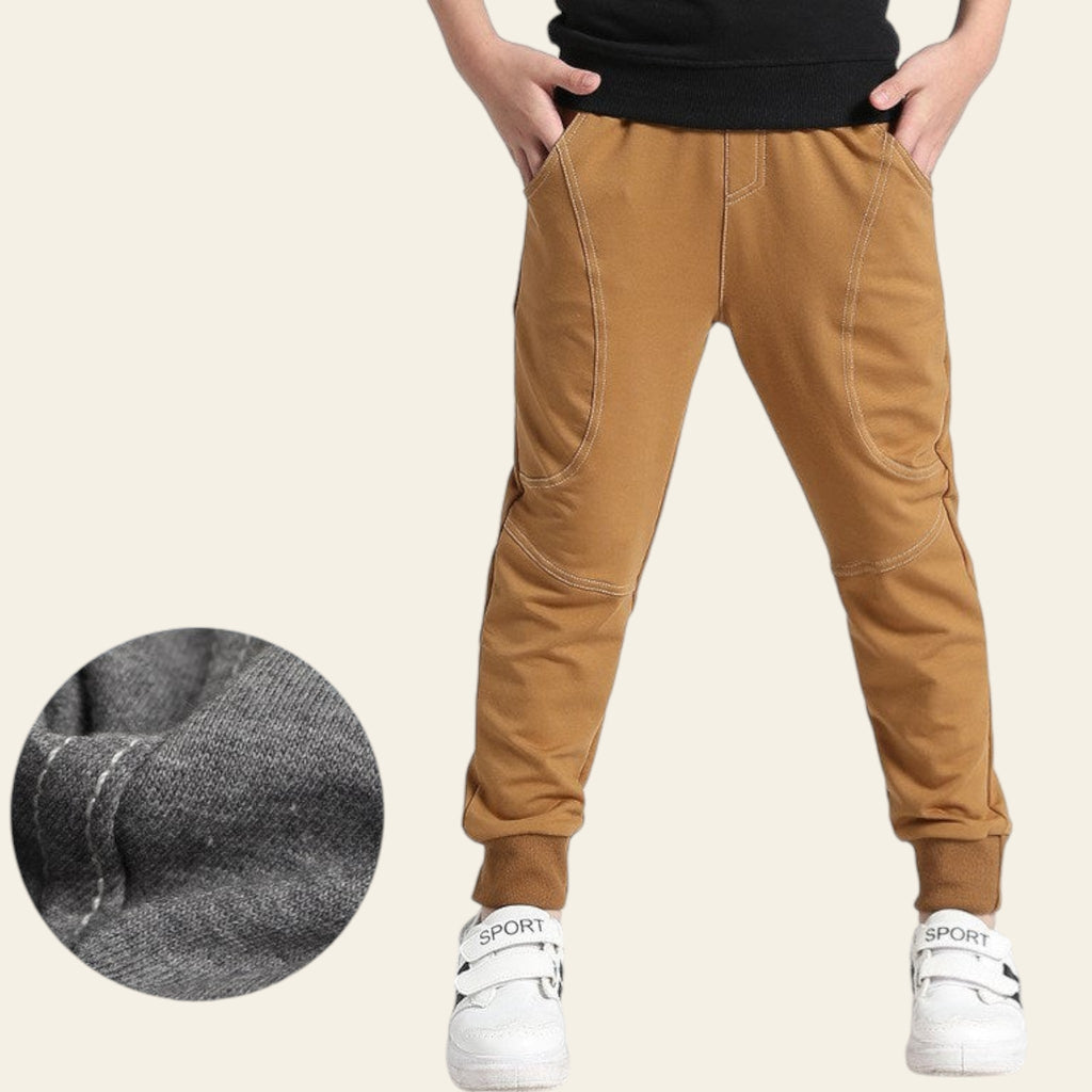 Brown jogger pants worn by a person on a white background with a close-up of fabric texture.