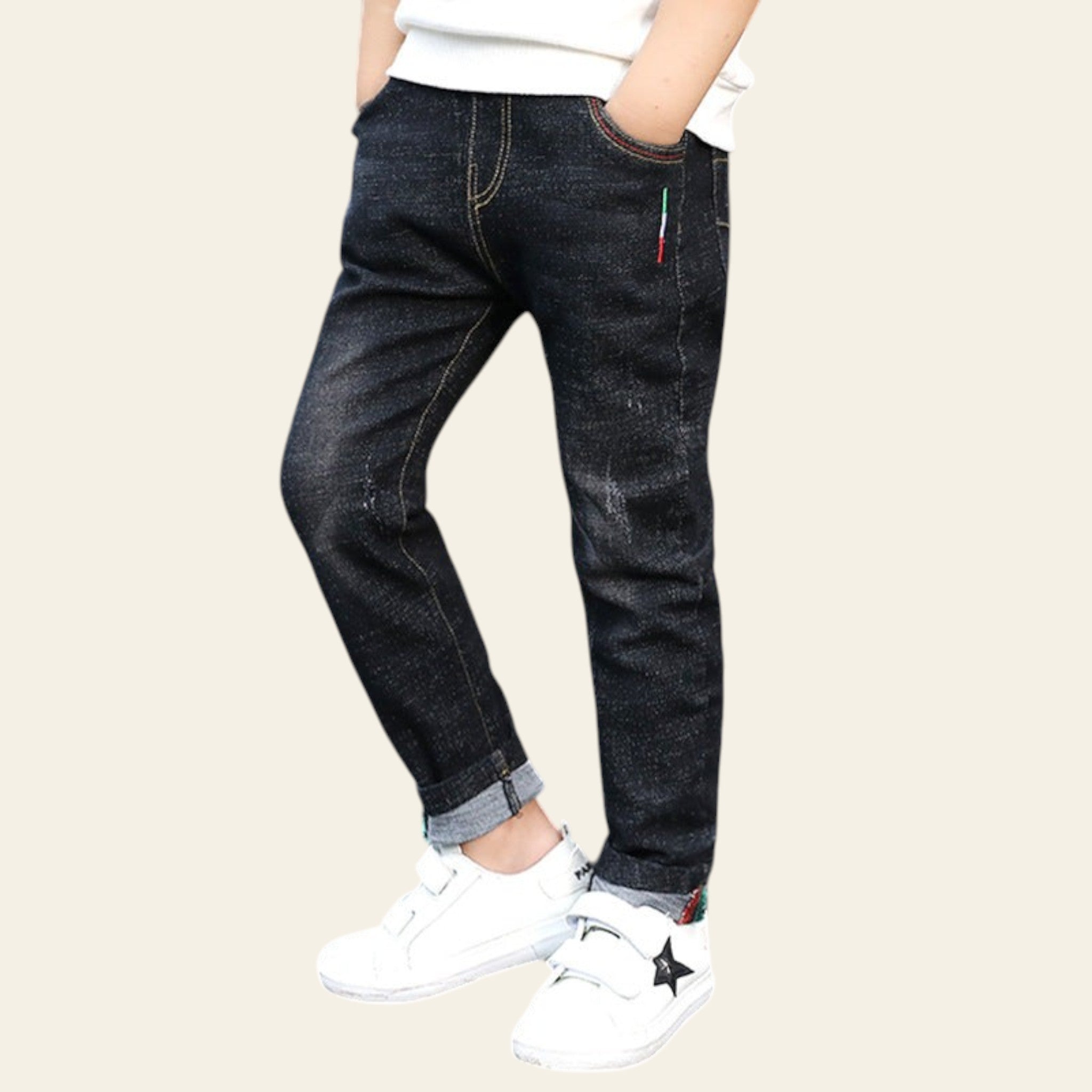 Person wearing dark jeans and white sneakers standing on a street with a yellow and black barrier in the background.