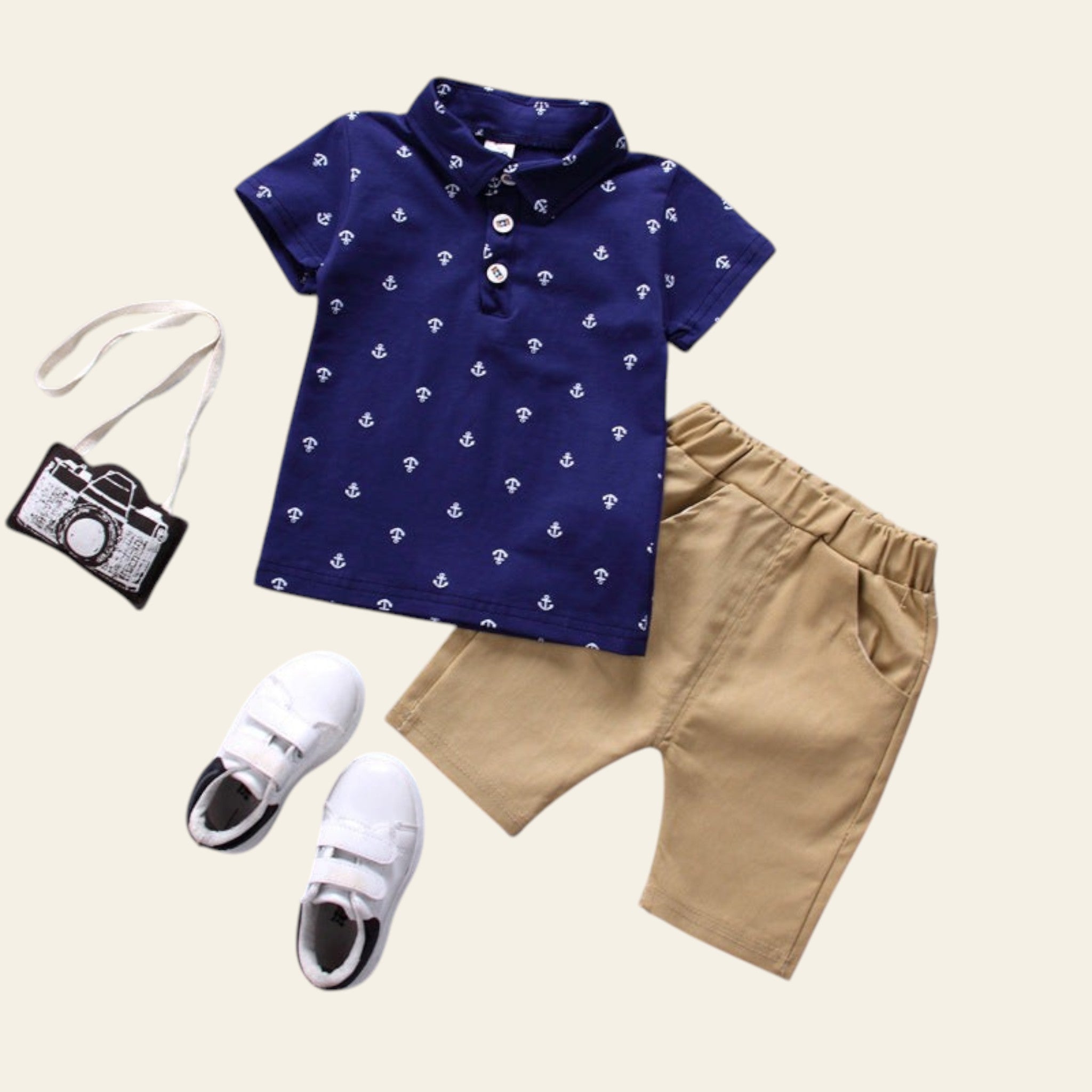 Children's outfit with navy shirt, beige shorts, white sneakers, and small camera bag on a gray background