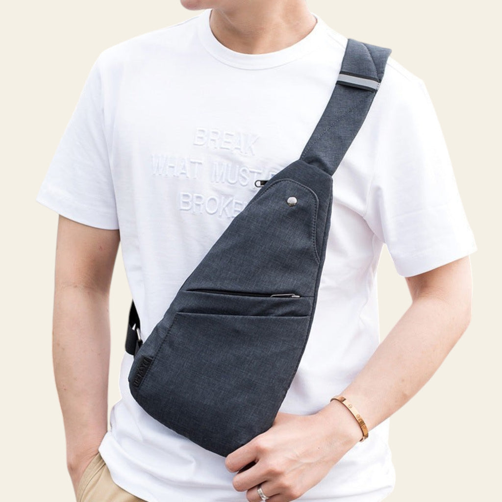 Person wearing a dark gray crossbody bag over one shoulder indoors.