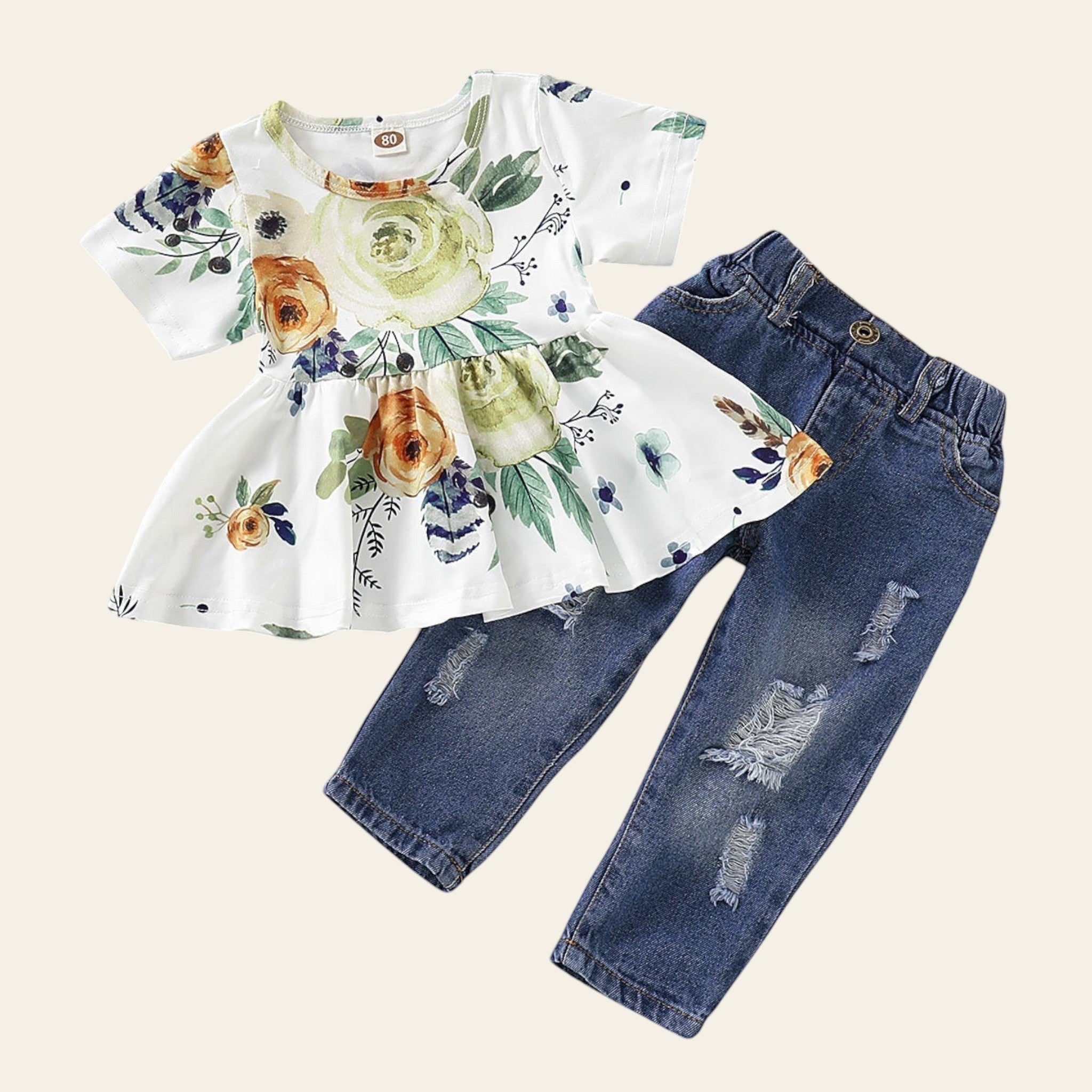 Children's outfit with floral top and ripped jeans on a wooden surface.