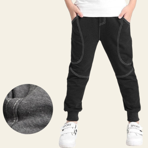 Black jogger pants with white sneakers on a light gray background