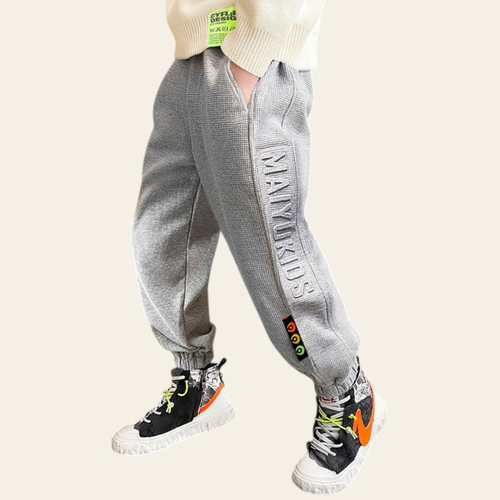 Person wearing gray jogger pants with branding and black sneakers in an indoor setting