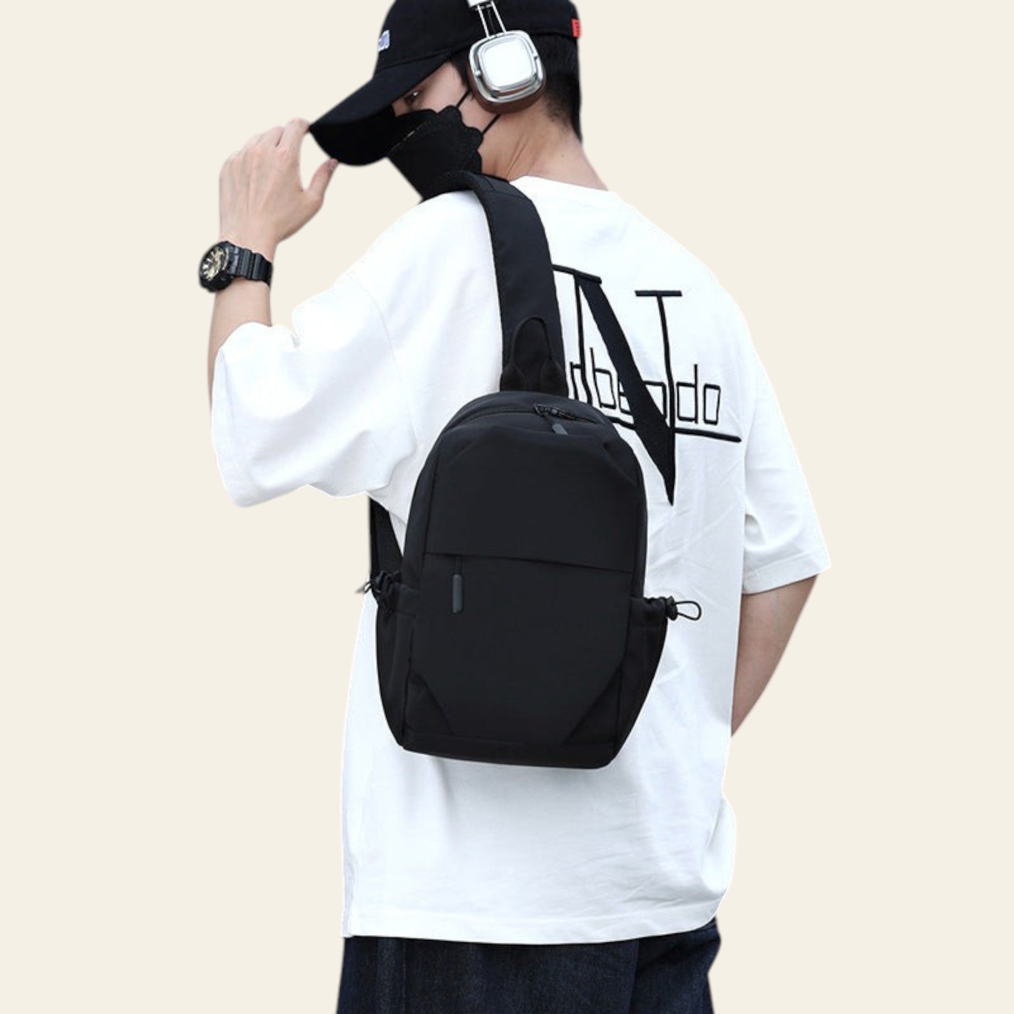 Person wearing a black backpack and white t-shirt with text, standing against a building.