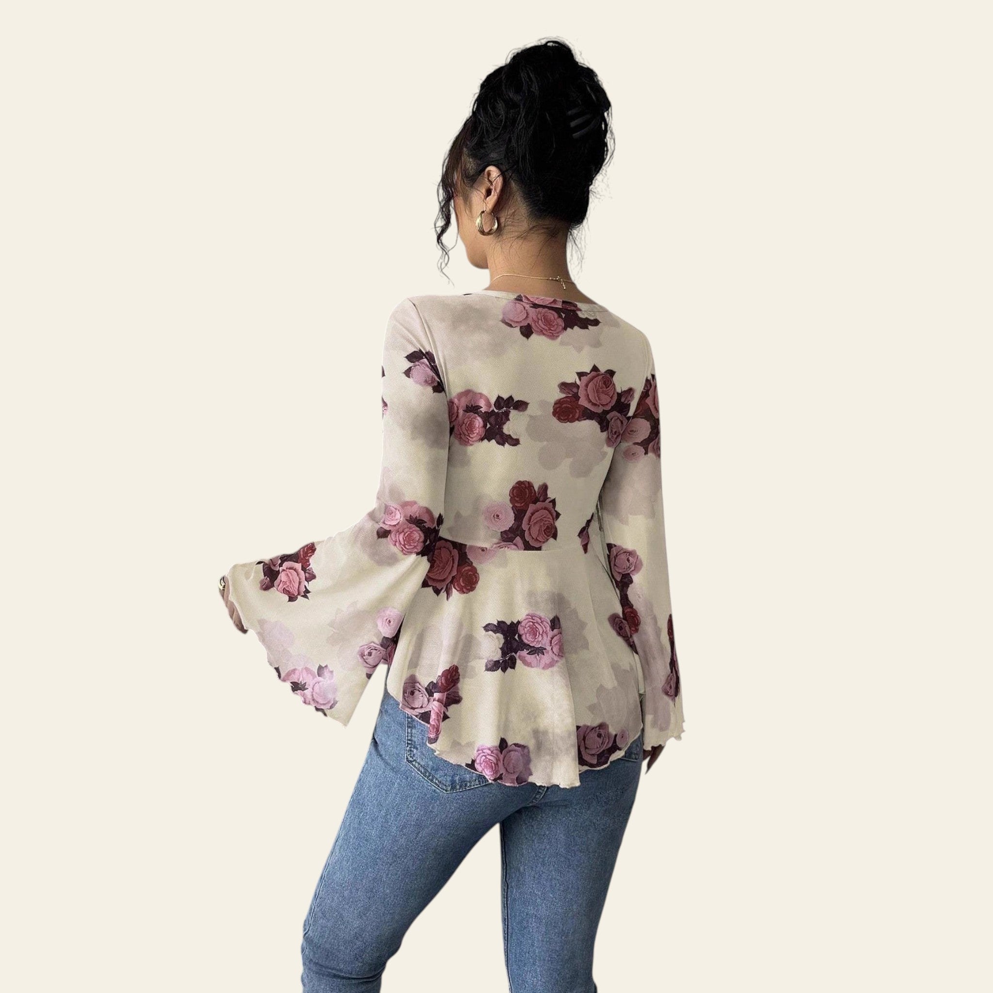 Person wearing a floral blouse with bell sleeves and blue jeans against a plain background