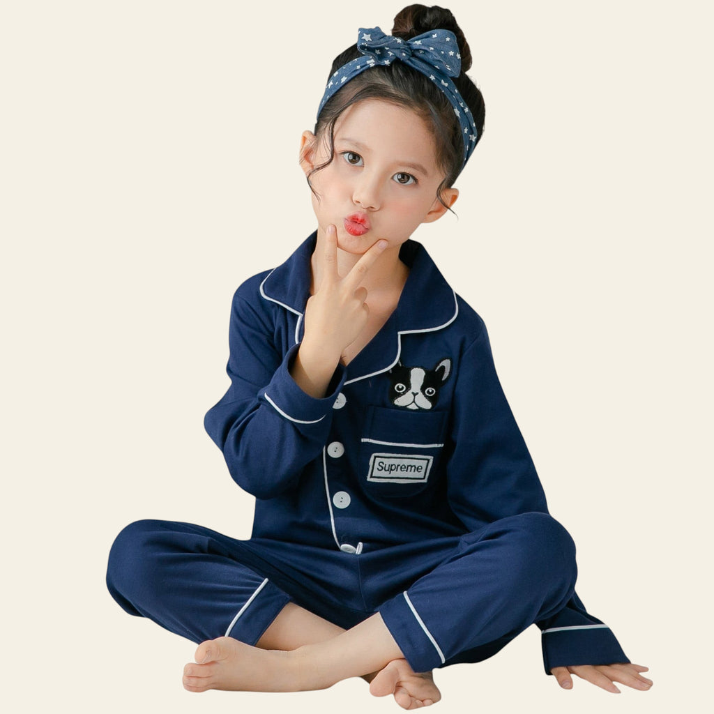 Child wearing a navy blue pajama set with a cat design, sitting on a bed.