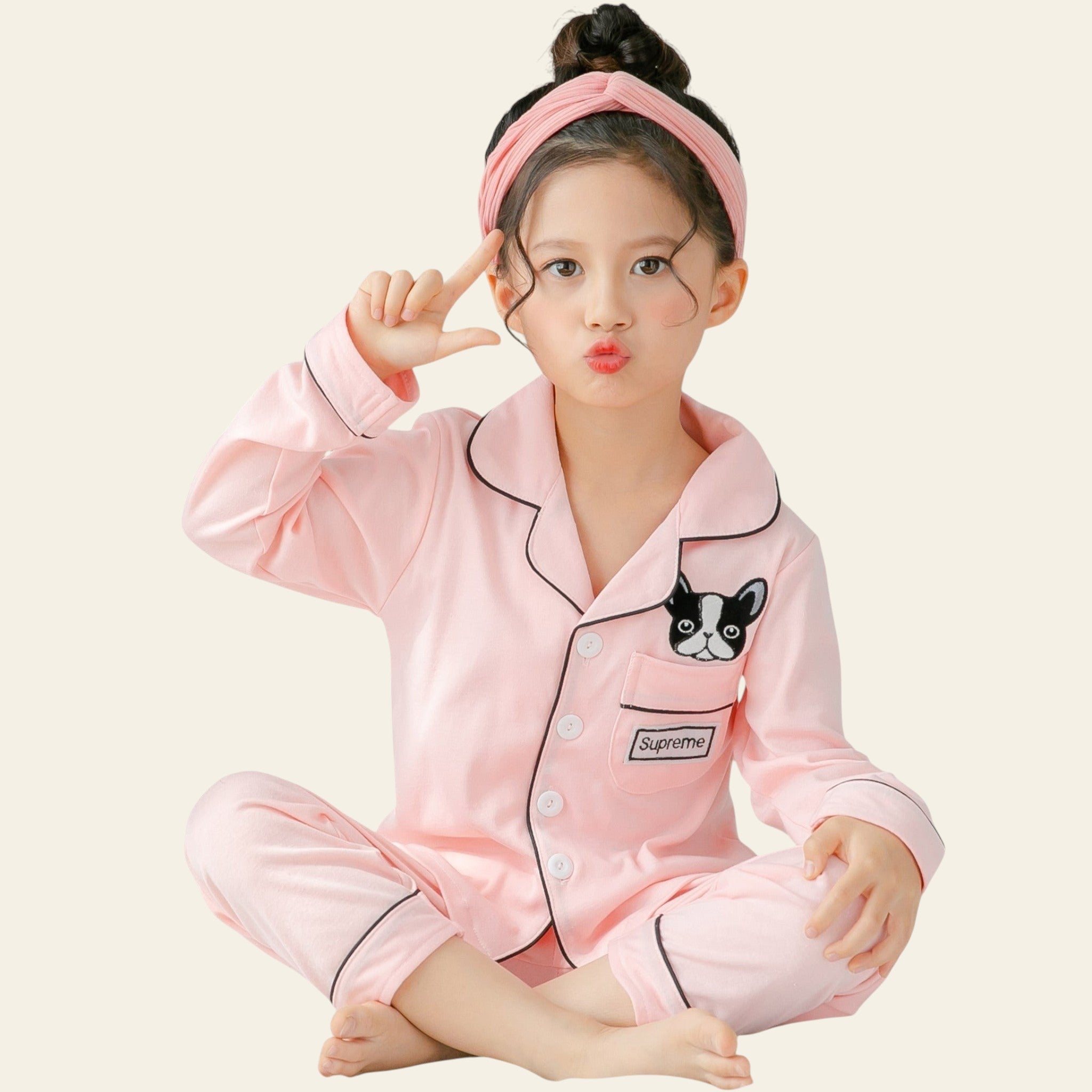 Child wearing pink pajamas with a dog design, sitting on a bed.