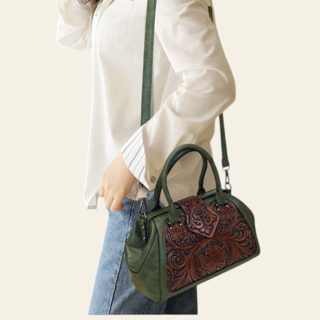 Green handbag with brown leather floral pattern held by a person wearing a white shirt and blue jeans.