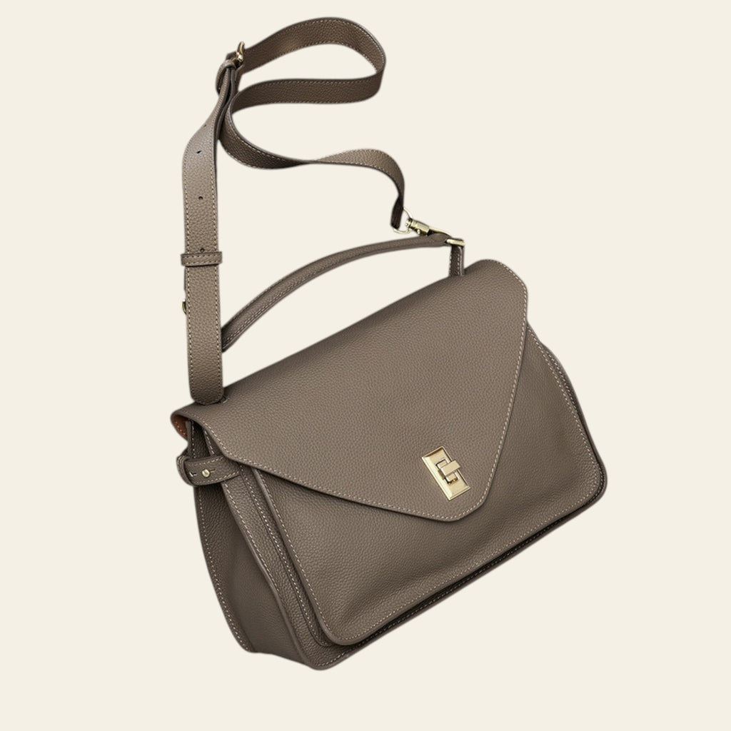 Brown leather handbag with a gold clasp on a light gray surface.