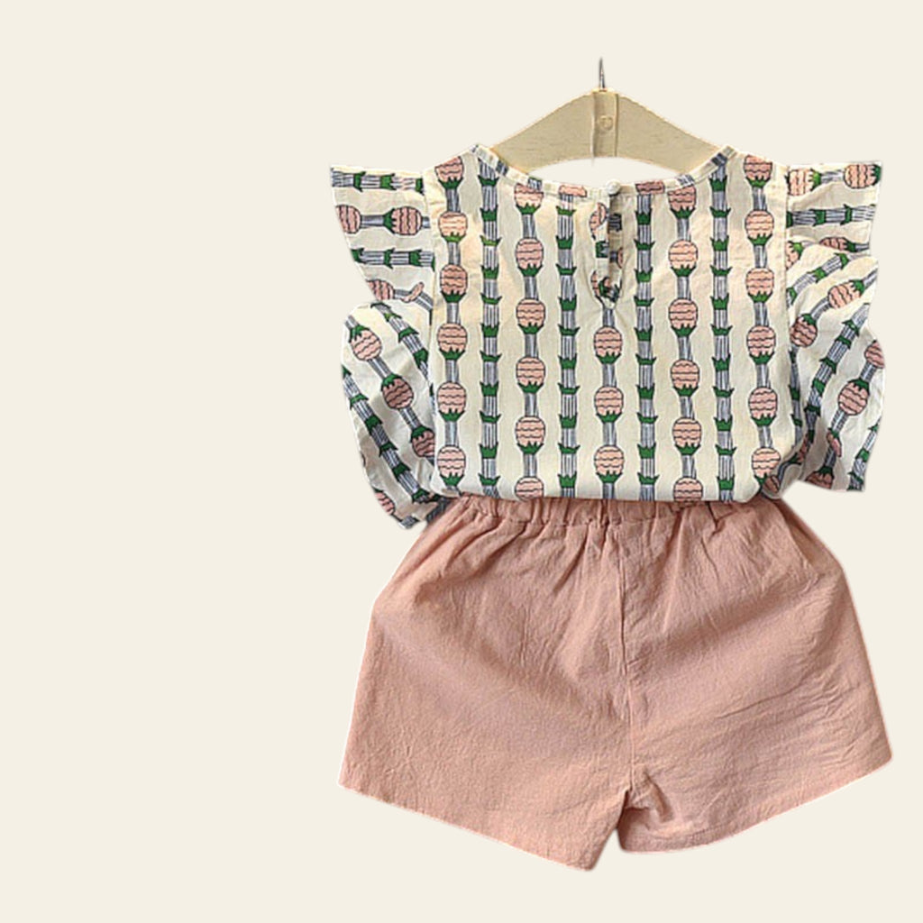 Children's outfit with patterned top and pink shorts on a dark surface with flowers.