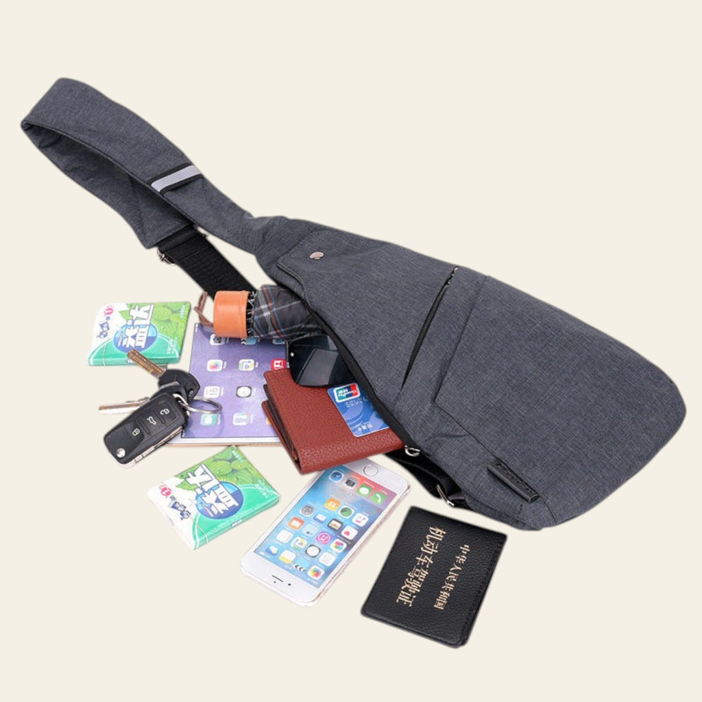 Gray crossbody bag with various items including a phone, wallet, and keys on a white background