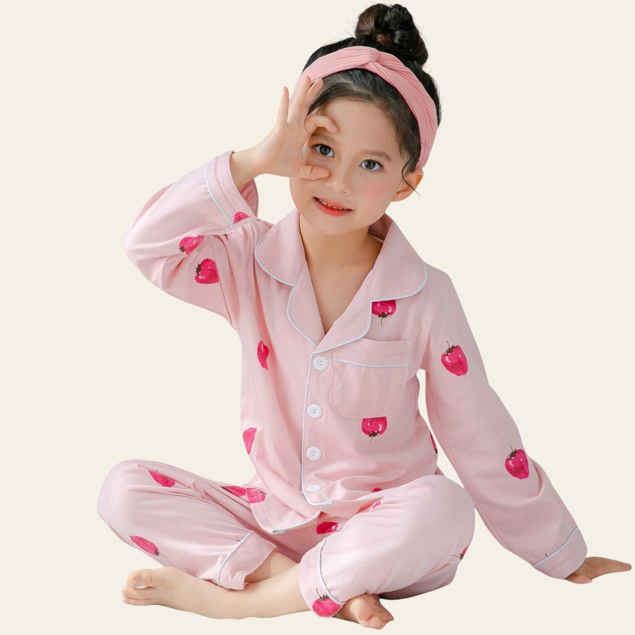 Child wearing pink pajamas with heart patterns on a bed.