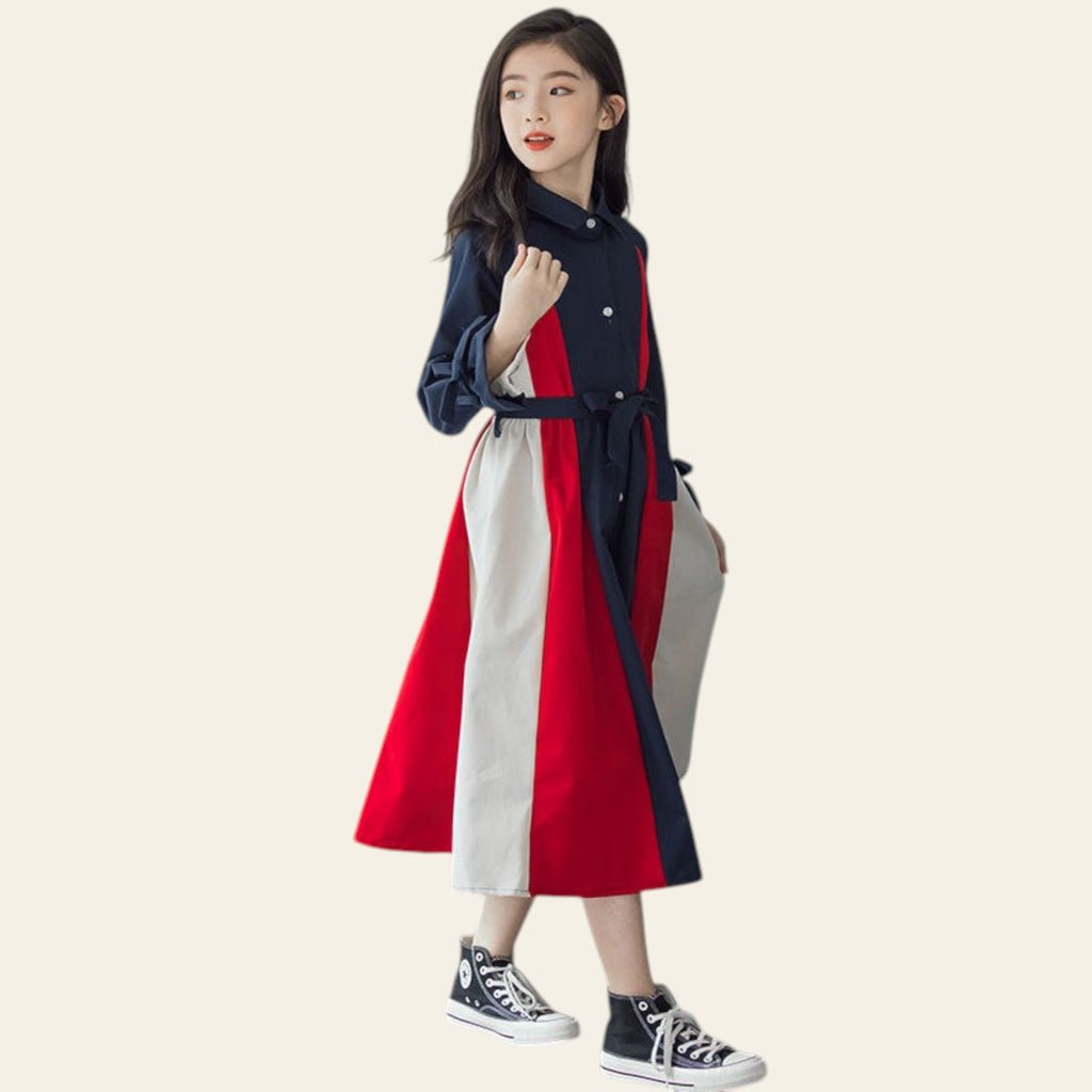 Woman wearing a red, white, and navy coat against a gray concrete wall.