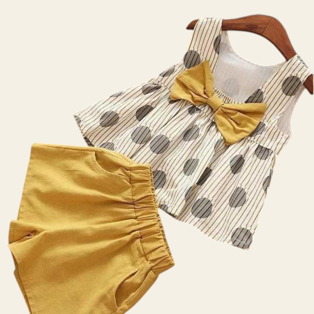 Children's outfit with polka dot top and yellow shorts on a wooden floor.