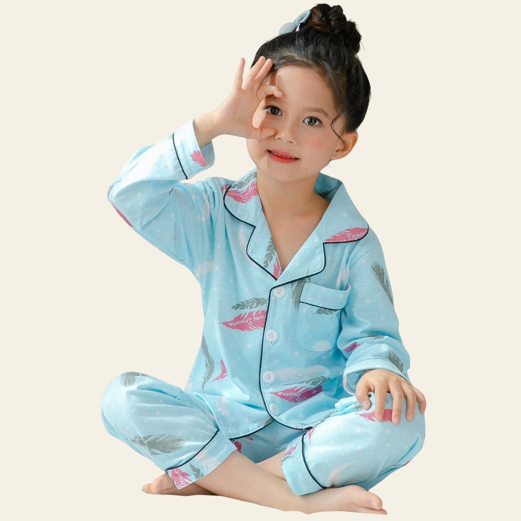 Child wearing light blue pajamas with pink accents, sitting on a bed.