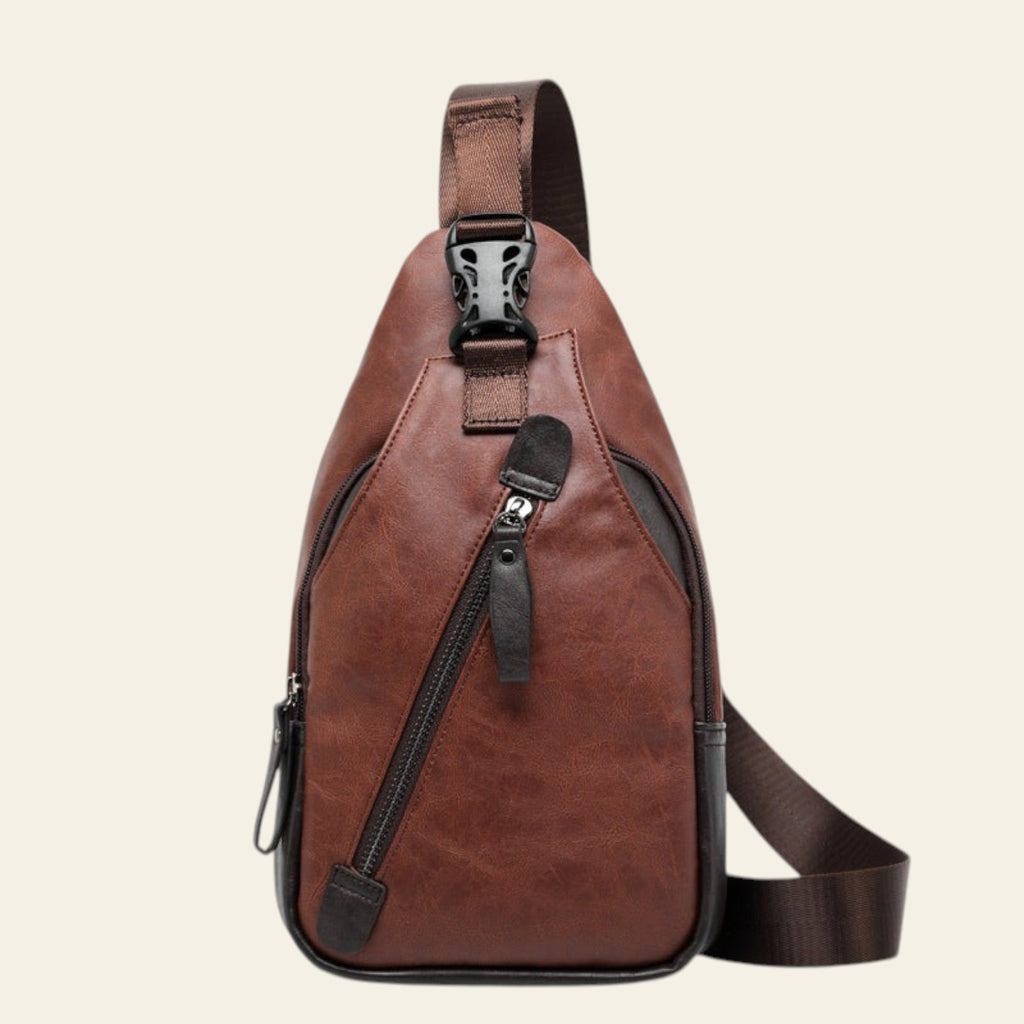 Brown leather sling bag with black zippers on a white background