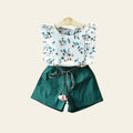 Children's outfit with floral top and green shorts on a gray background