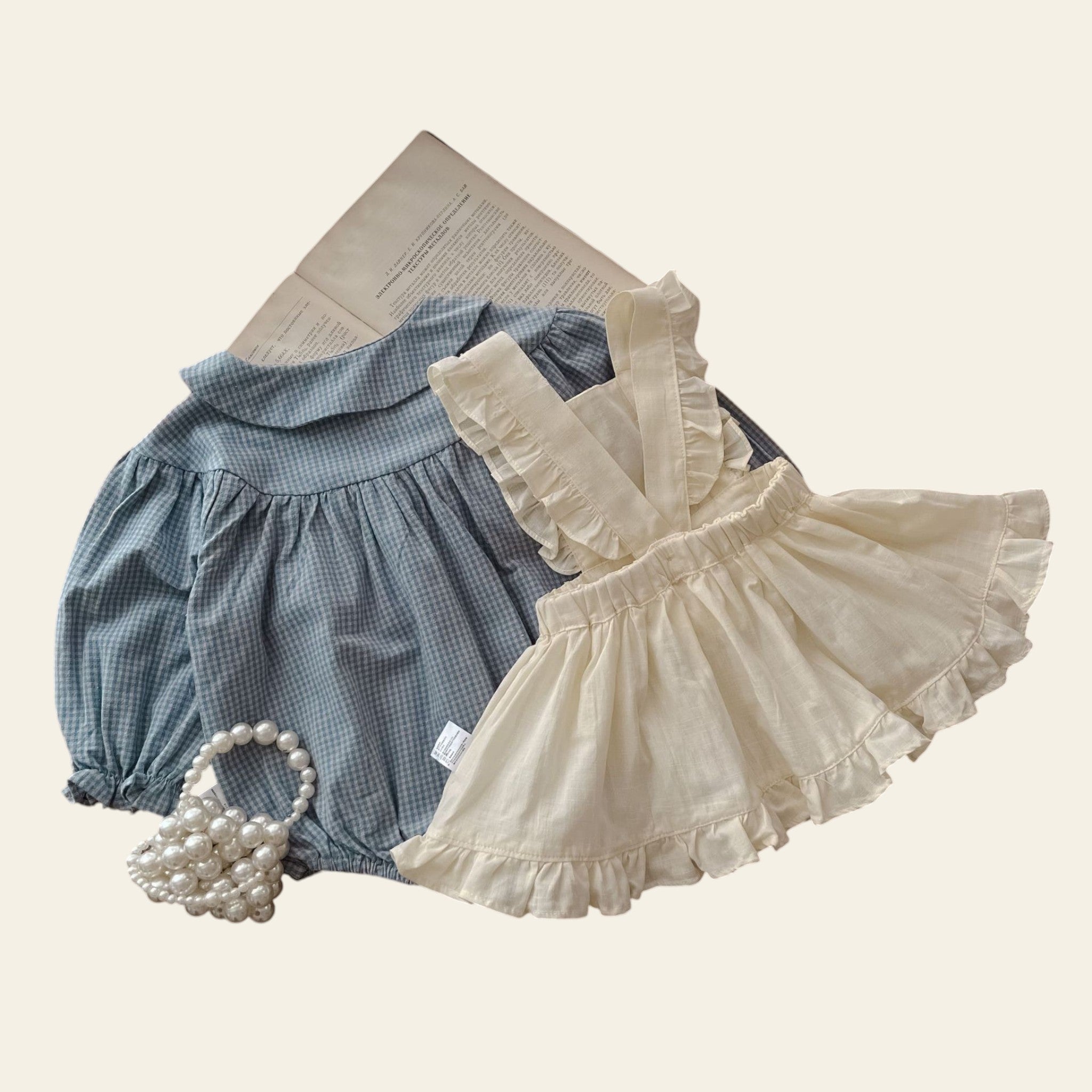 Children's blue checkered outfit and white ruffled dress on a wooden surface.