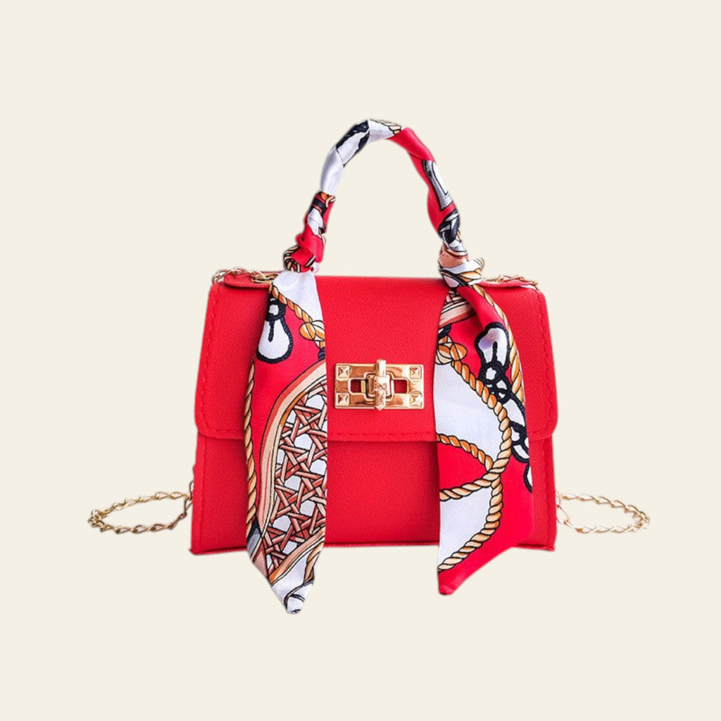Red handbag with a decorative scarf draped over it on a white background
