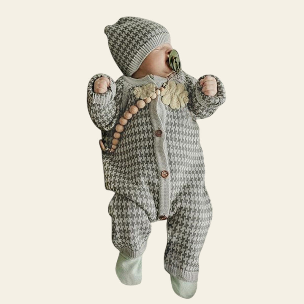 Baby in a knitted outfit with a hat lying on a textured blanket