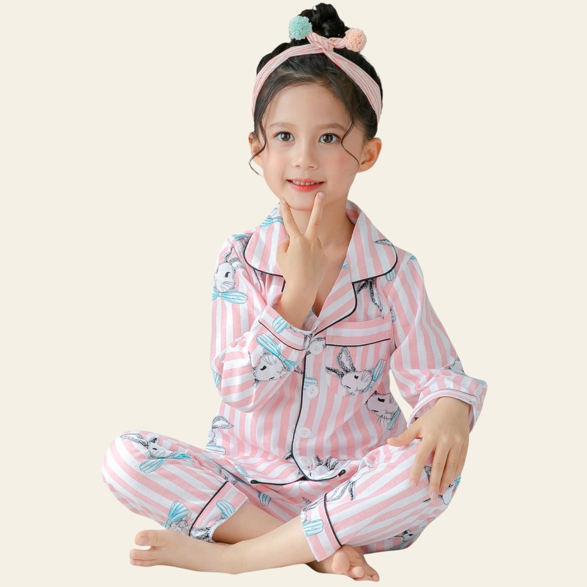 Child wearing pink striped pajamas with cartoon designs on a white bed.