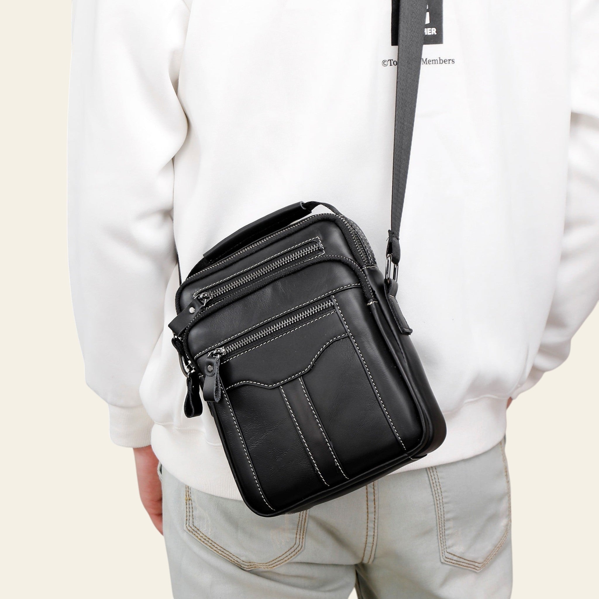 Person wearing a black crossbody bag with a plain background