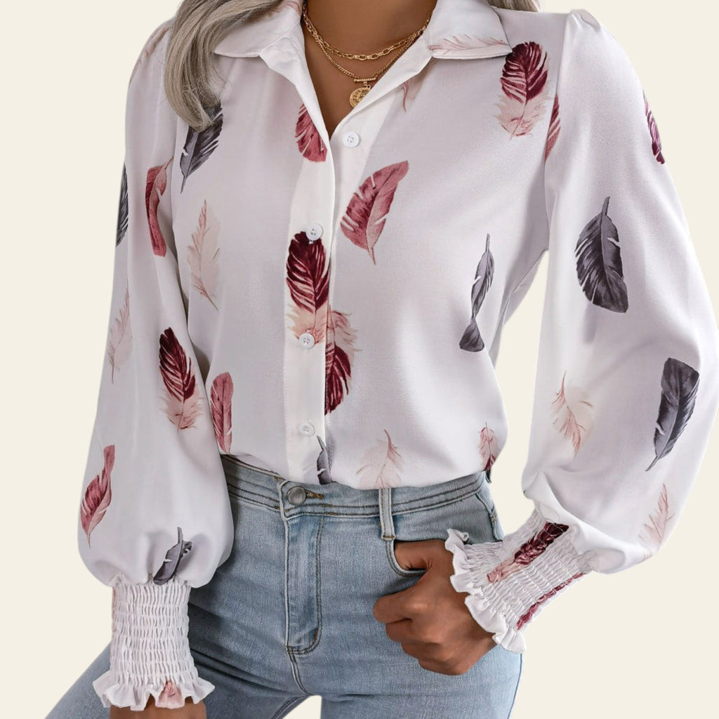 Woman wearing a white blouse with floral patterns and light blue jeans indoors.